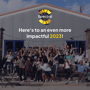 Fifth and last slide of the impact report. Spectral's logo and the text "Here's to an even more impactful 2023!" are shown over a photo of the Spectral team in front of a large barn. About 60 people are shown in the photo, in excited poses with their arms stretched out and smiles on their faces. The people shown have various skin colors, genders, and ages.